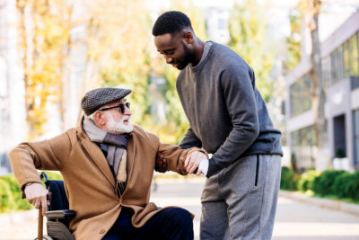young african american cuidador helping senior disabled man